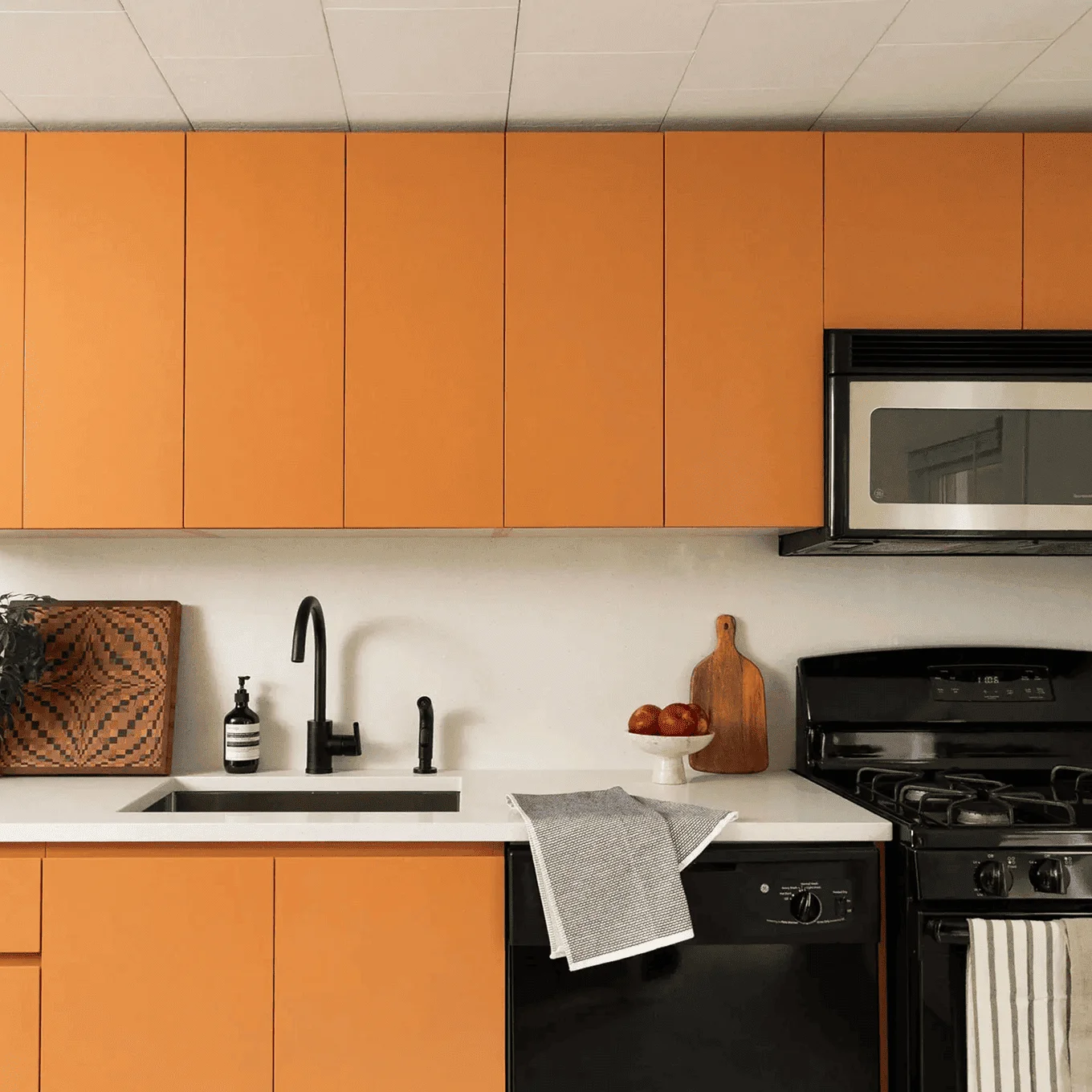 Modern kitchen featuring flat‑panel burnt‑orange cabinets, white quartz countertop, matte‑black faucet, and black gas range, part of a complete home renovation on Walling St, Sayreville NJ