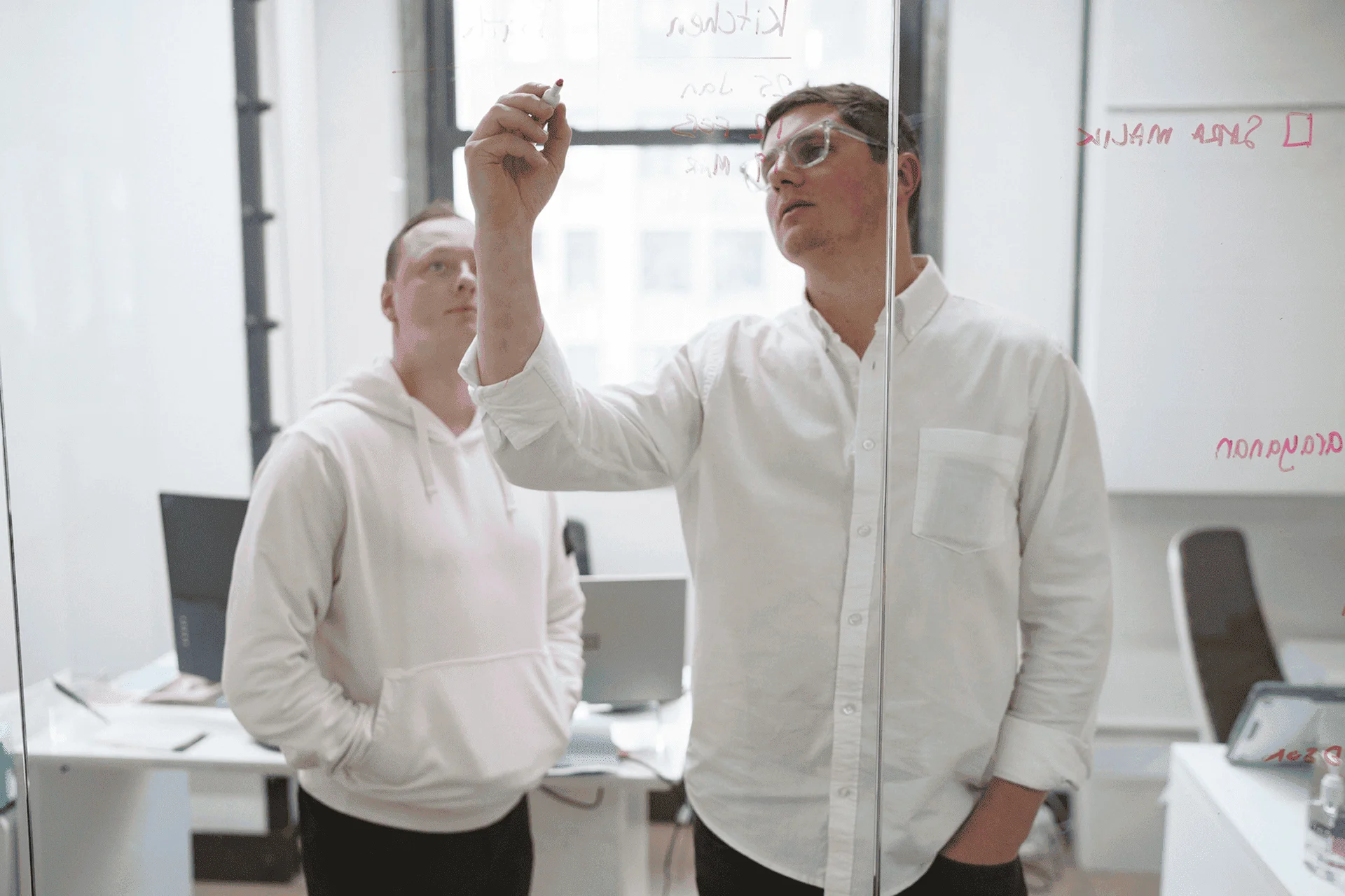 Two Chapter team members collaborate in a modern office, one writing planning notes on a glass wall while the other observes.