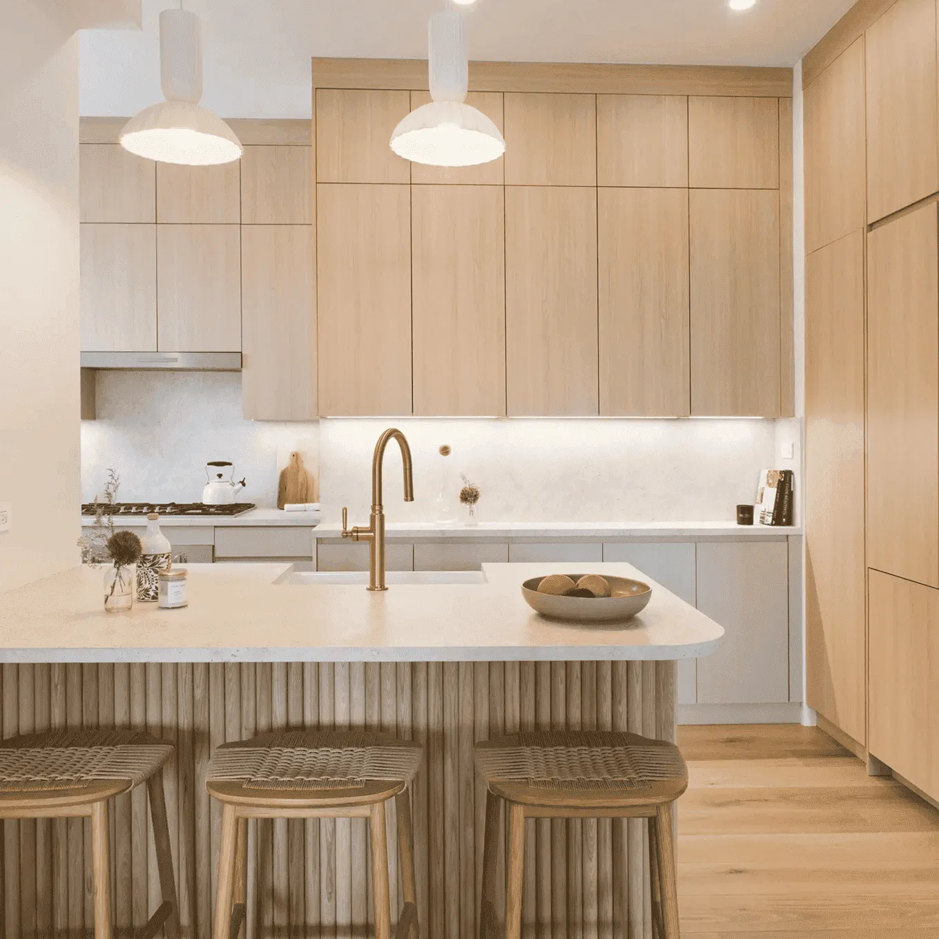 Modern kitchen with light-wood cabinets, marble island, woven stools, and brass faucet in a Tribeca renovation by Chapter.