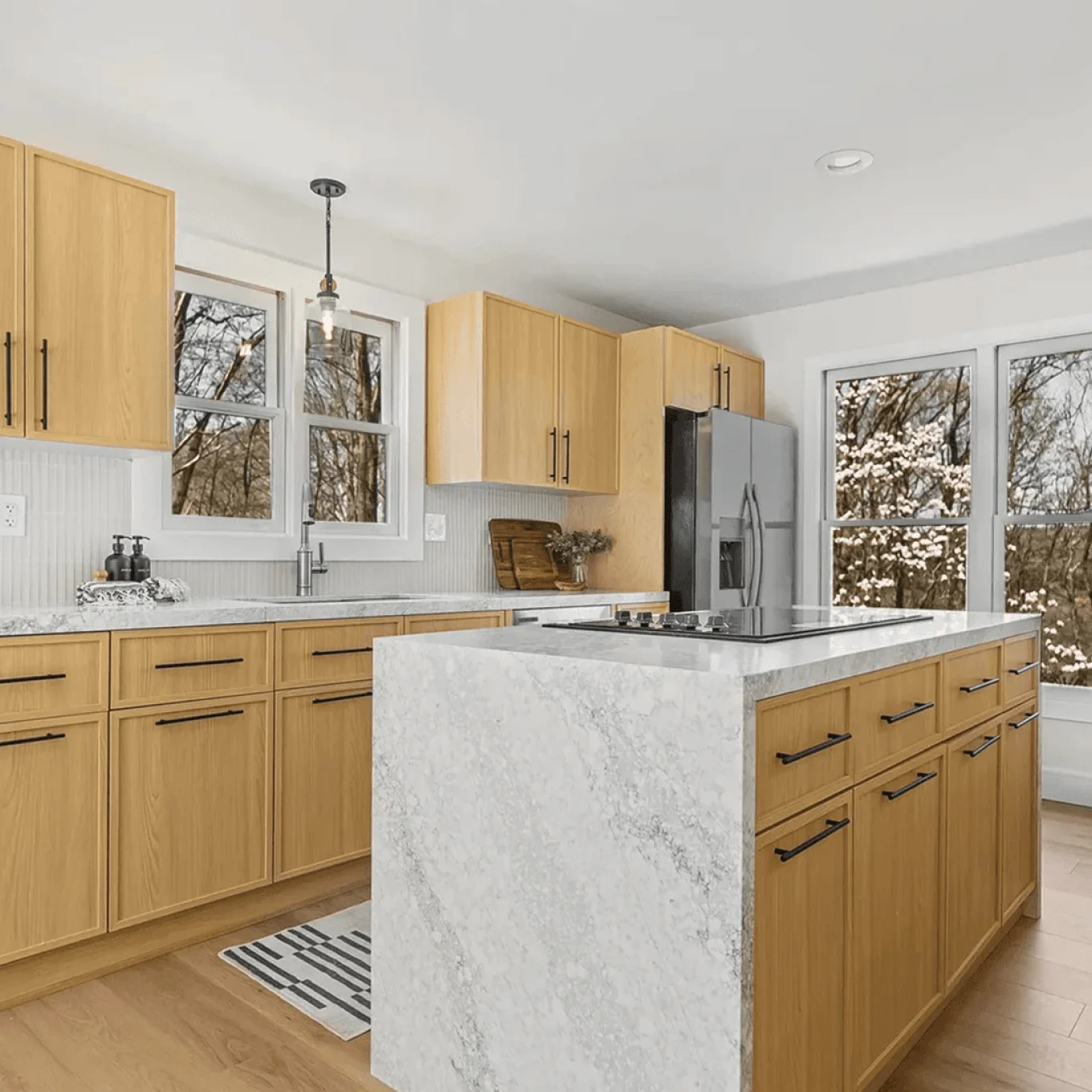 Wide view of renovated kitchen featuring farmhouse sink, wood lower cabinets, stainless appliances and arched openings to bright dining area in Connecticut.