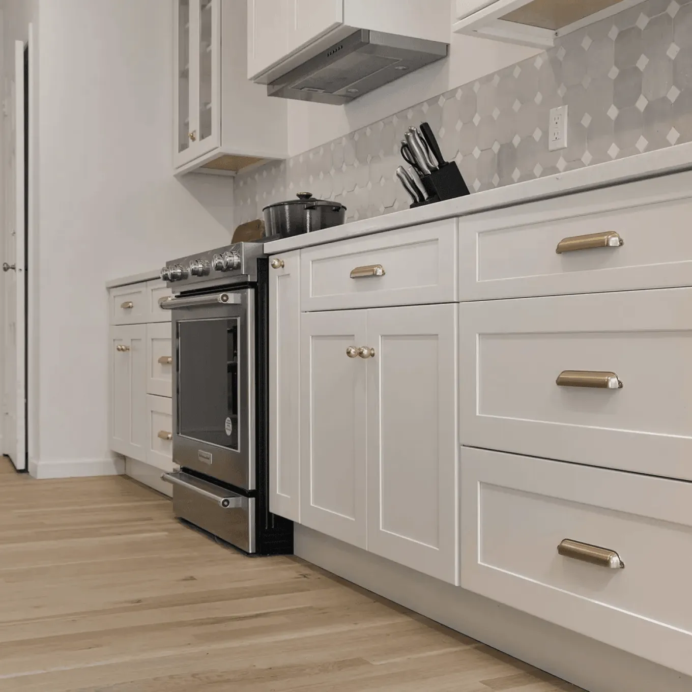 Modern Westchester kitchen with large marble island and wood base, white shaker cabinets with glass-front uppers, patterned tile backsplash and center cooktop.