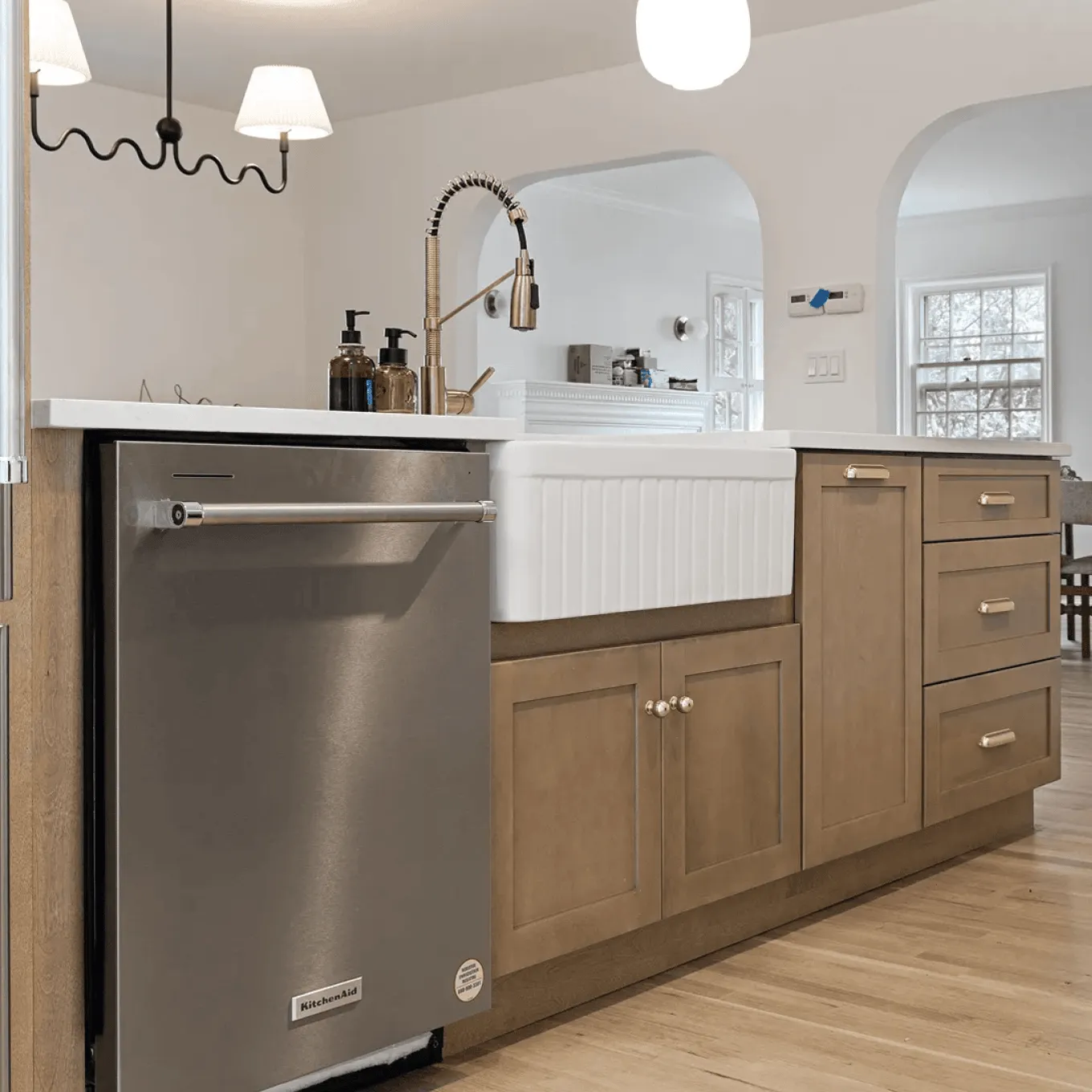 Wide view of renovated kitchen featuring farmhouse sink, wood lower cabinets, stainless appliances and arched openings to bright dining area in Westchester, NY.