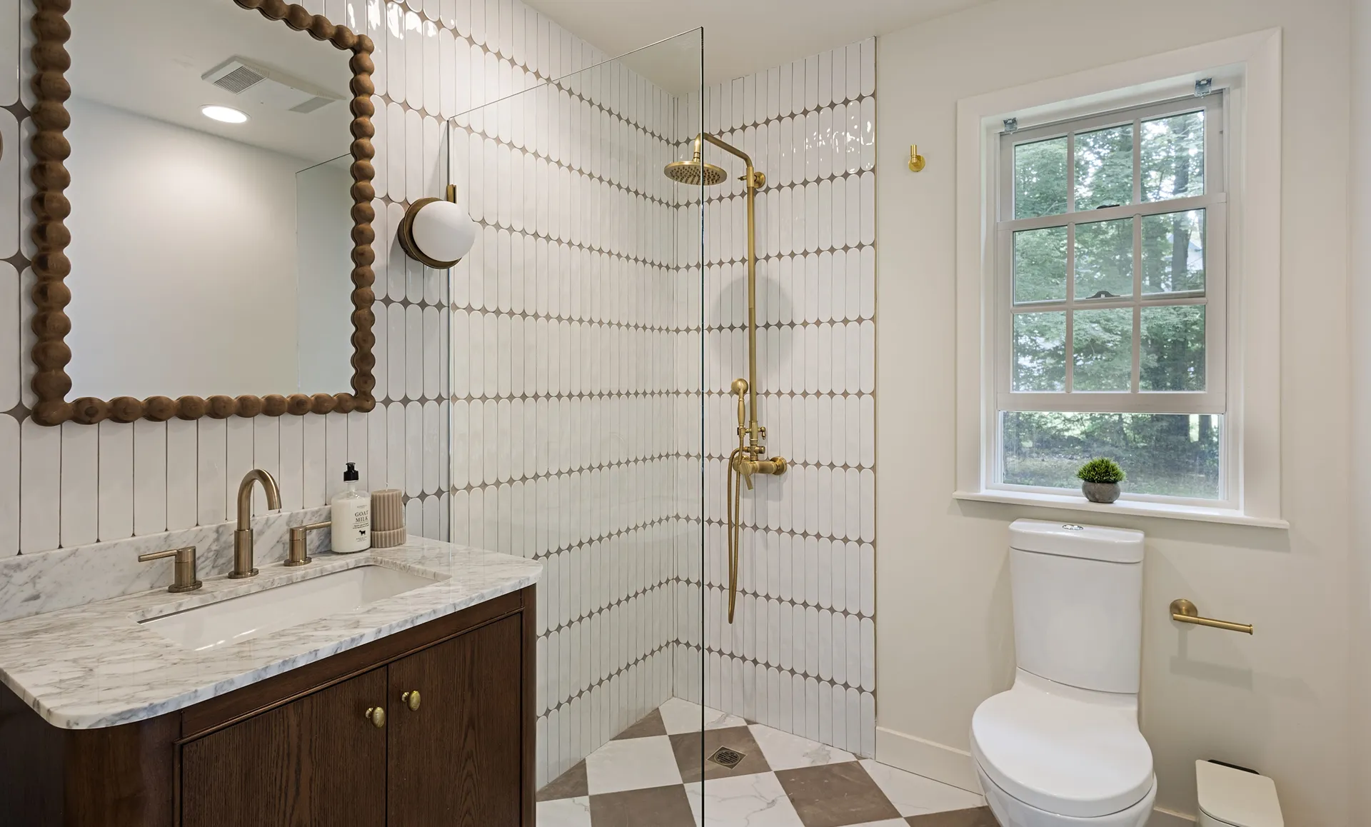 Bathroom with vertical vertically aligned tiles, brown-and-white checkered floor, brass fixtures, bead-framed mirror and marble vanity.