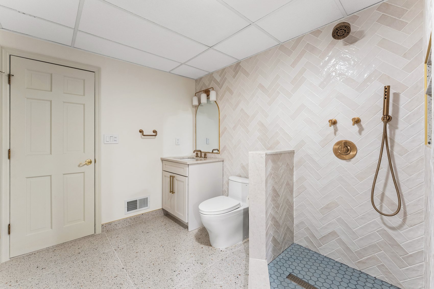 After view of the basement guest bathroom with light stone tile, shower, toilet, and updated fixtures.
