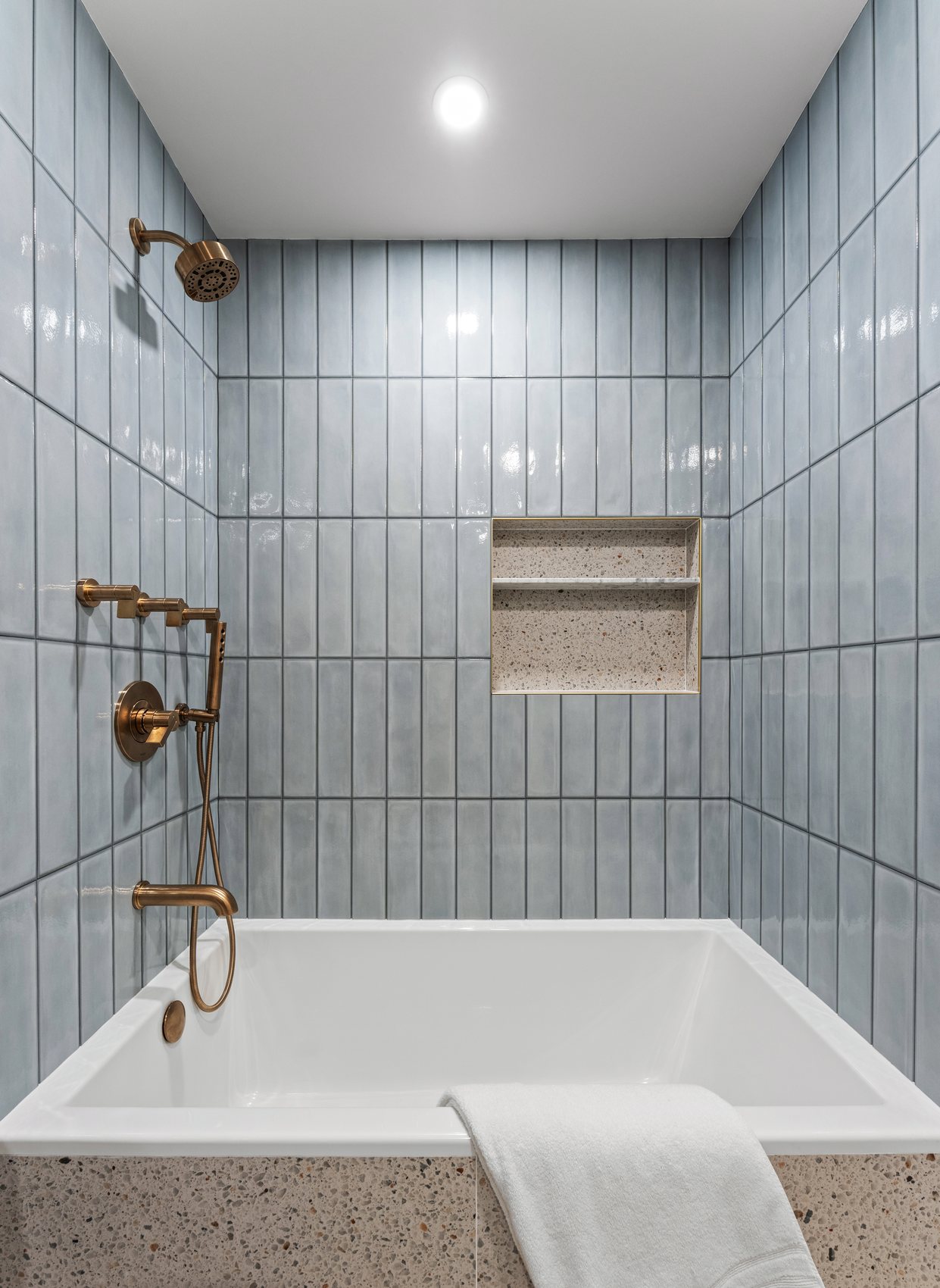 Blue bathroom tile with brass shower fixtures and bathtub.