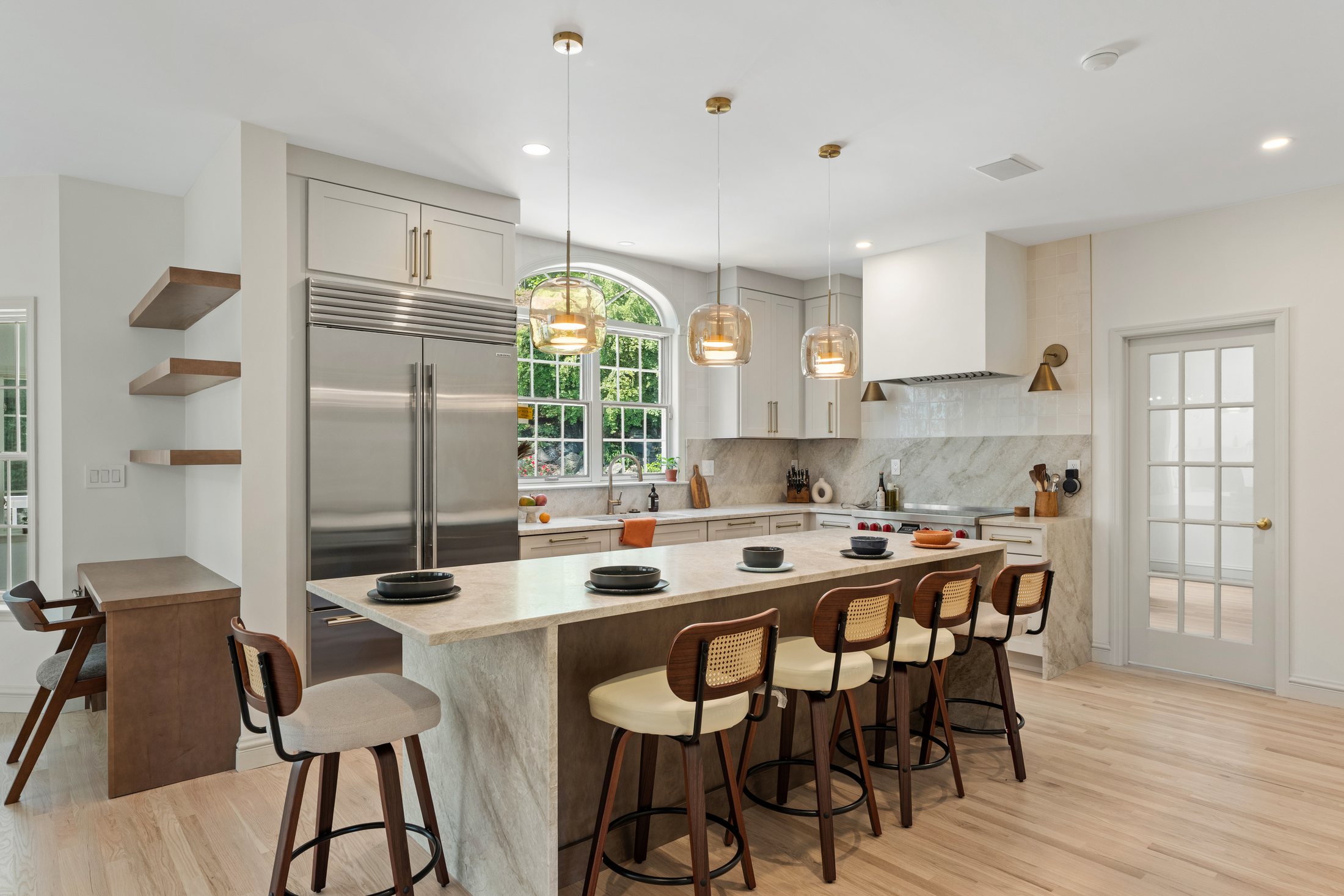 Finished Briarcliff Manor kitchen with a large quartzite island, warm wood cabinetry, brass fixtures, pendant lights, and integrated refrigeration.