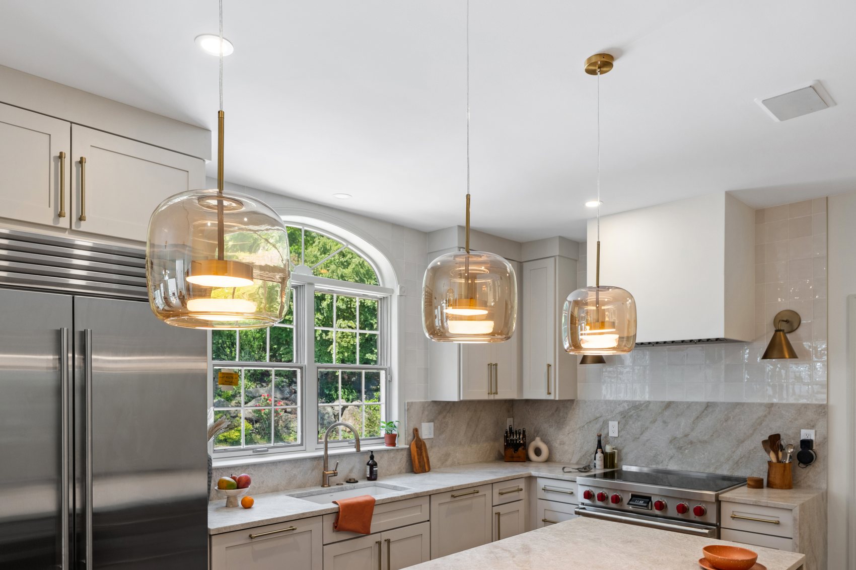 Wide view of the finished kitchen with light oak flooring, arched window, pendant lights, and quartzite island.