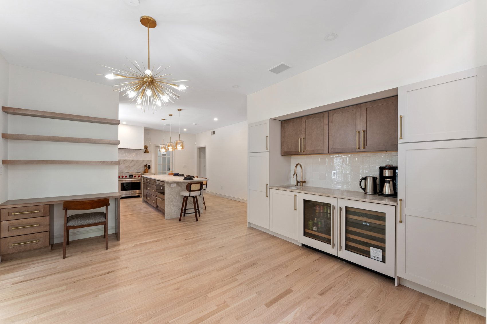 Renovated kitchen and adjacent workspace with light oak floors, beverage station, desk nook, and custom storage.