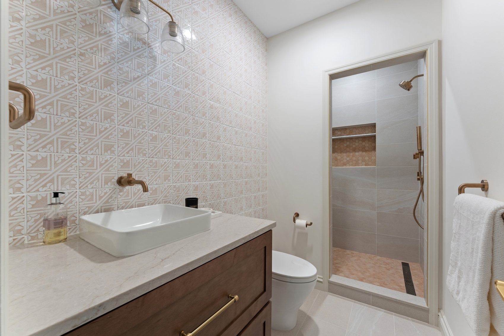 After view of the powder room converted to a full bathroom with patterned tile, shower, and wood vanity.