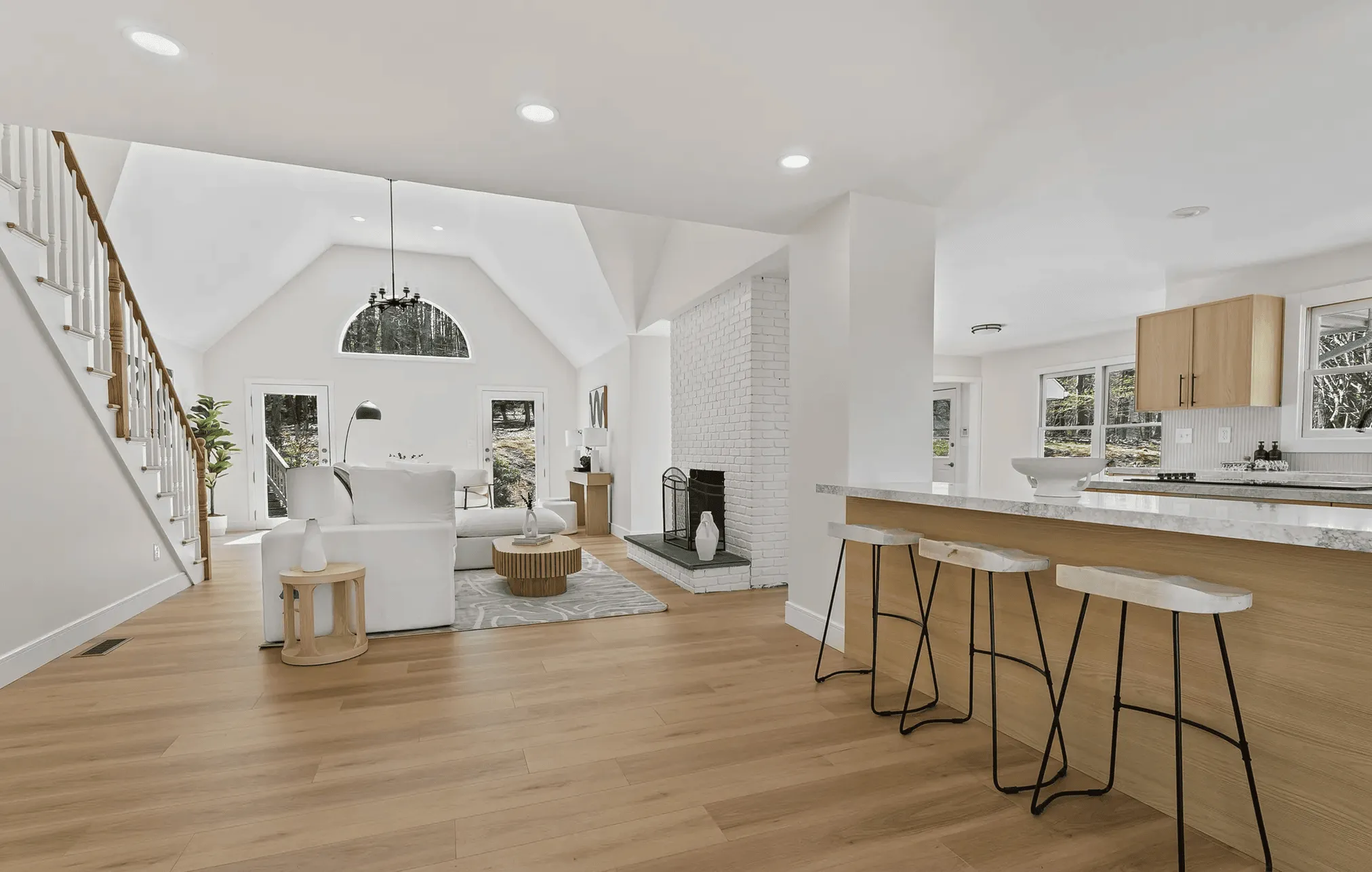 Bright open-concept living room and kitchen with vaulted ceiling, wood floors, white sofa, quartz island and white bar stools, part of a full house renovation on Greens Farms Road, Westport, CT