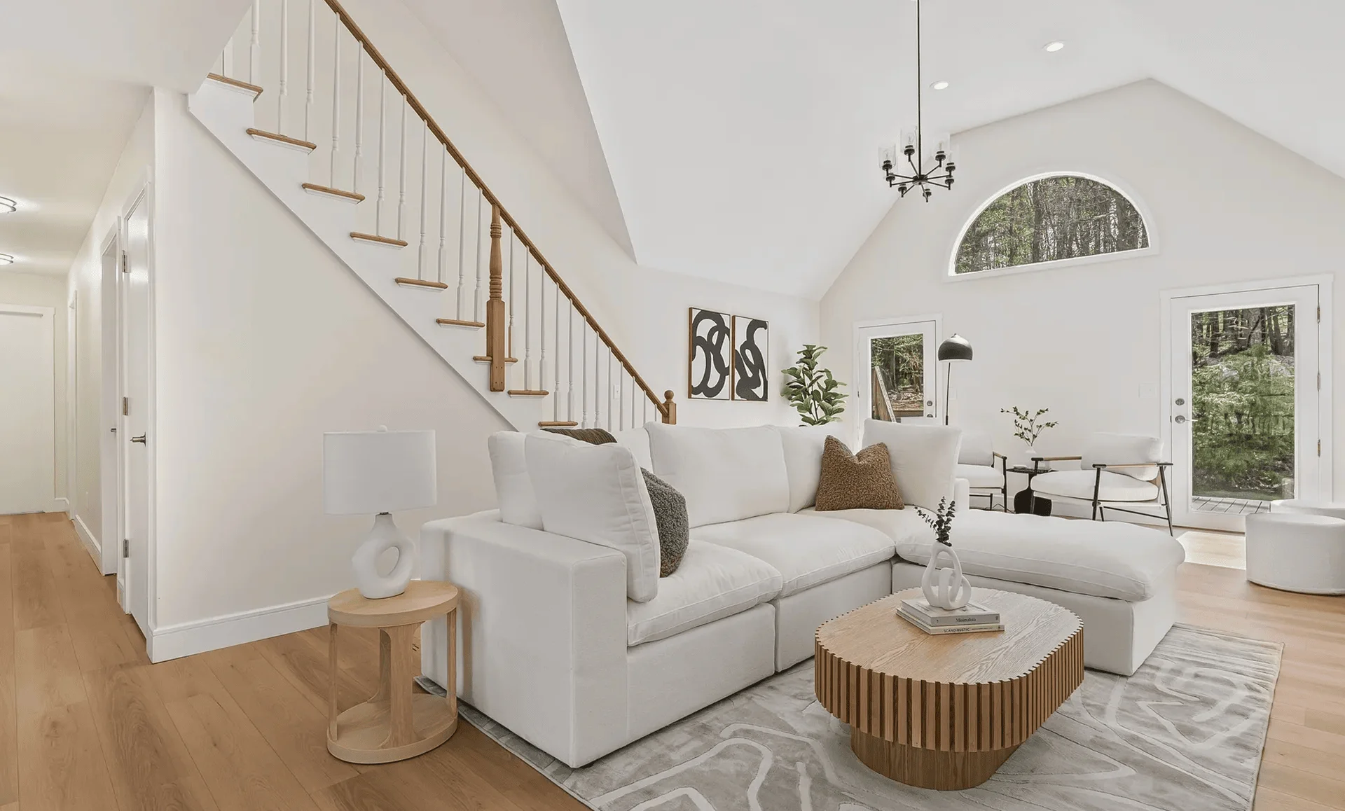Living area with white sofa, oak floors and open staircase showing airy layout and abundant natural light.