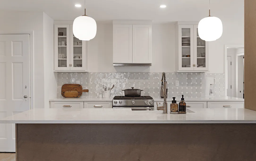 Modern New Rochelle kitchen with large marble island and wood base, white shaker cabinets with glass-front uppers, patterned tile backsplash and center cooktop.