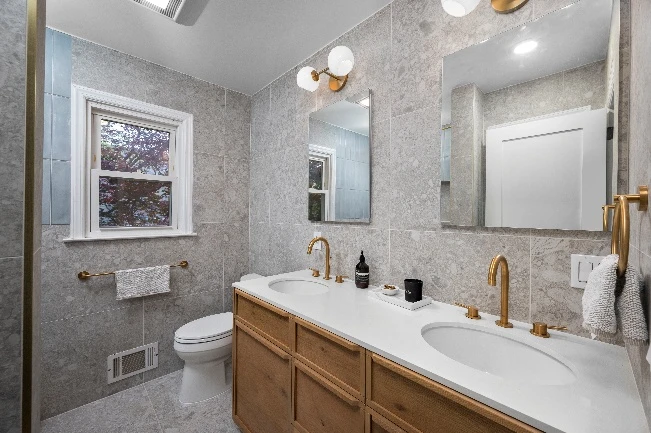 Renovated kids bathroom in Rye home with terrazzo-inspired flooring, glossy blue wall tile, and gold fixtures
