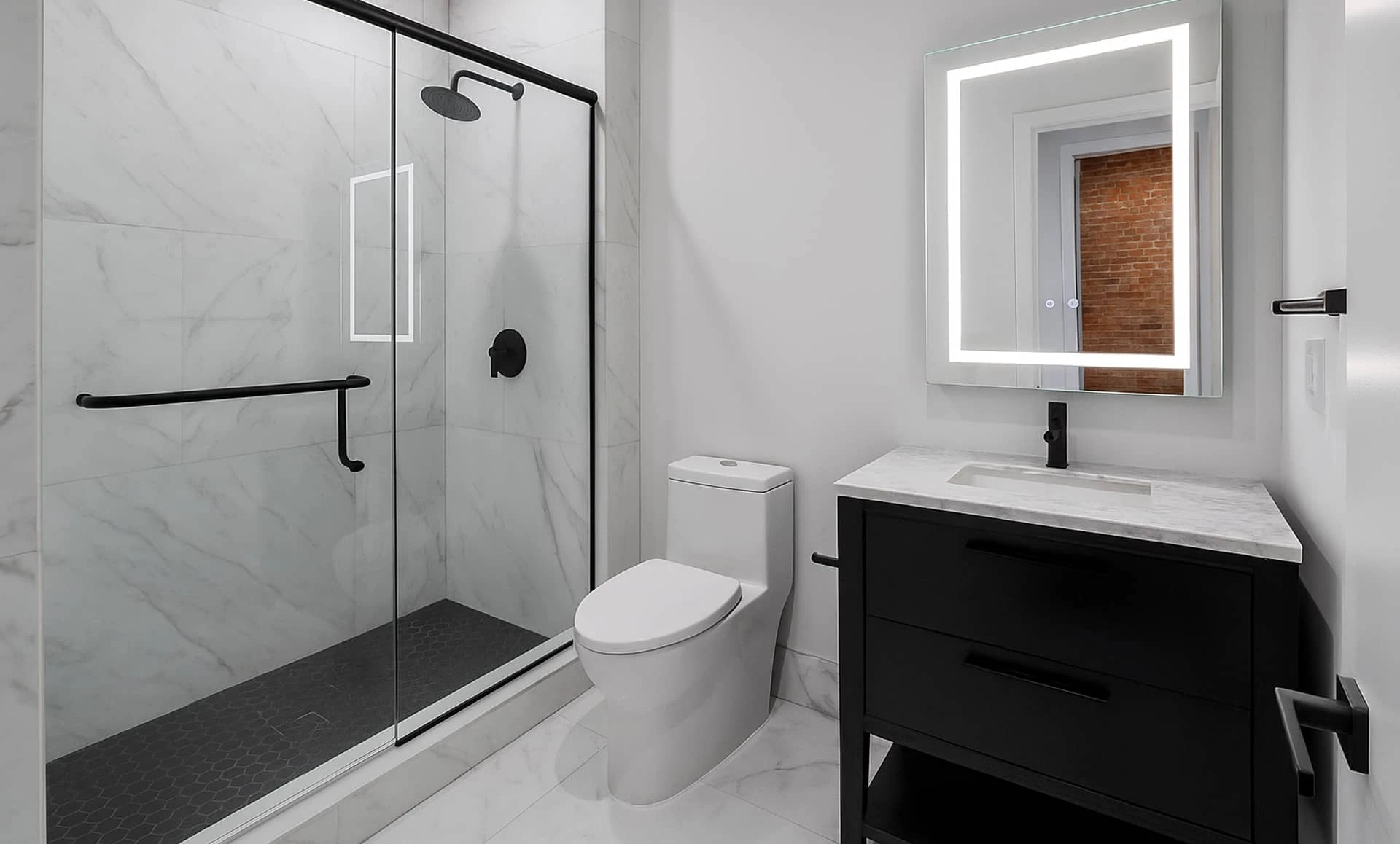 Modern dark brown-and-white bathroom featuring glass walk-in shower, matte-black fixtures, LED mirror and marble-topped vanity.