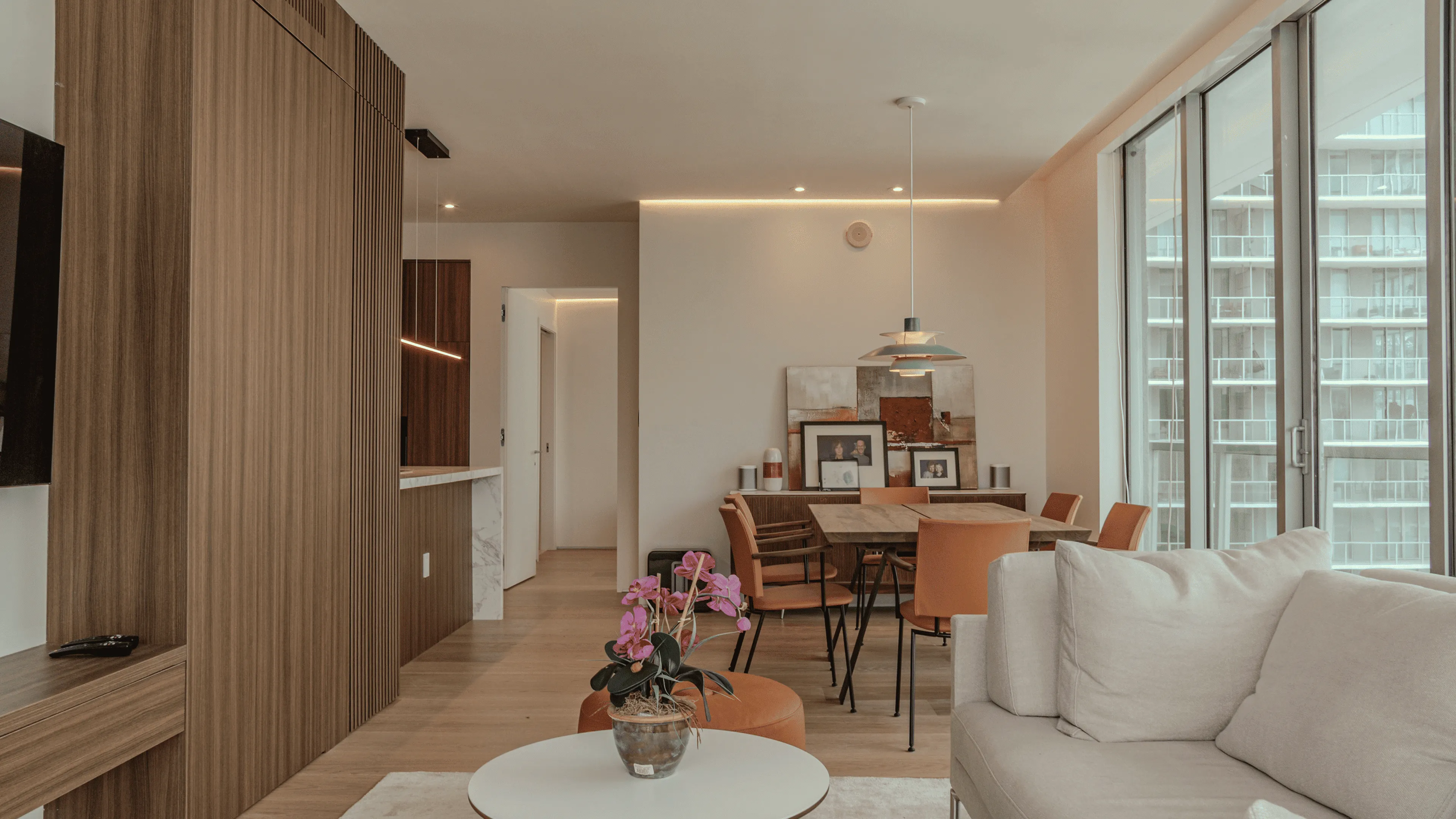 Modern open-concept living and dining area in a renovated Axis Brickell condo apartment, featuring custom wood wall paneling, floor-to-ceiling windows, light-toned sofa, and contemporary decor.