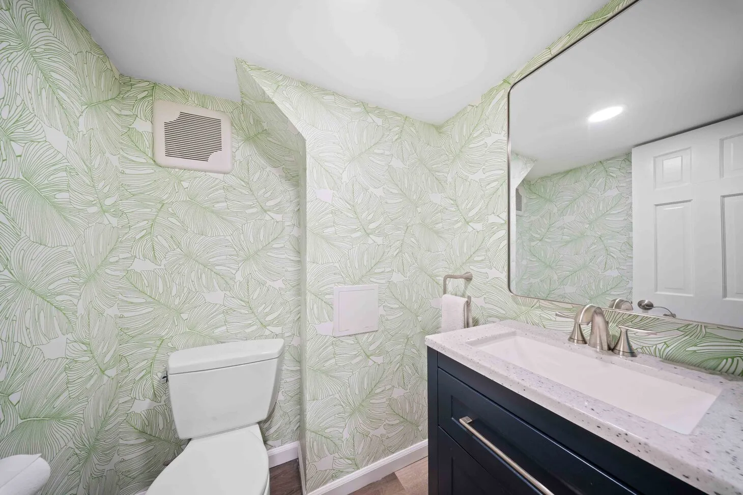 Basement powder room with tropical leaf wallpaper, navy vanity, and white quartz top