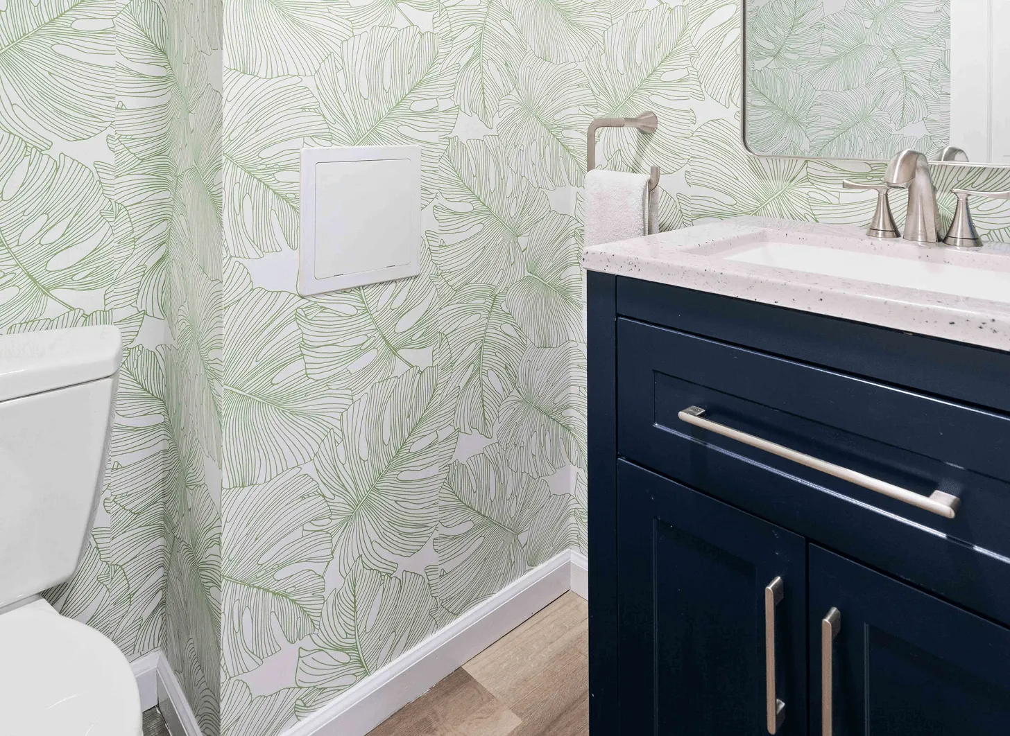 Renovated Maplewood basement powder room with tropical leaf wallpaper, navy vanity, and white quartz countertop