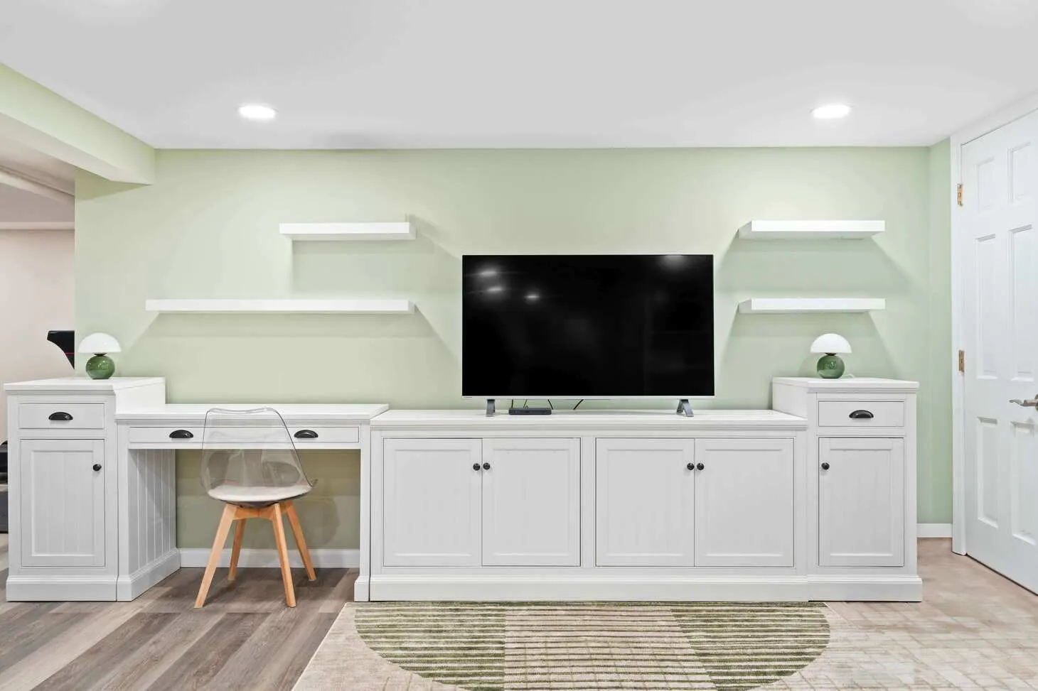 Custom white basement built-ins with TV, floating shelves, and sage green wall