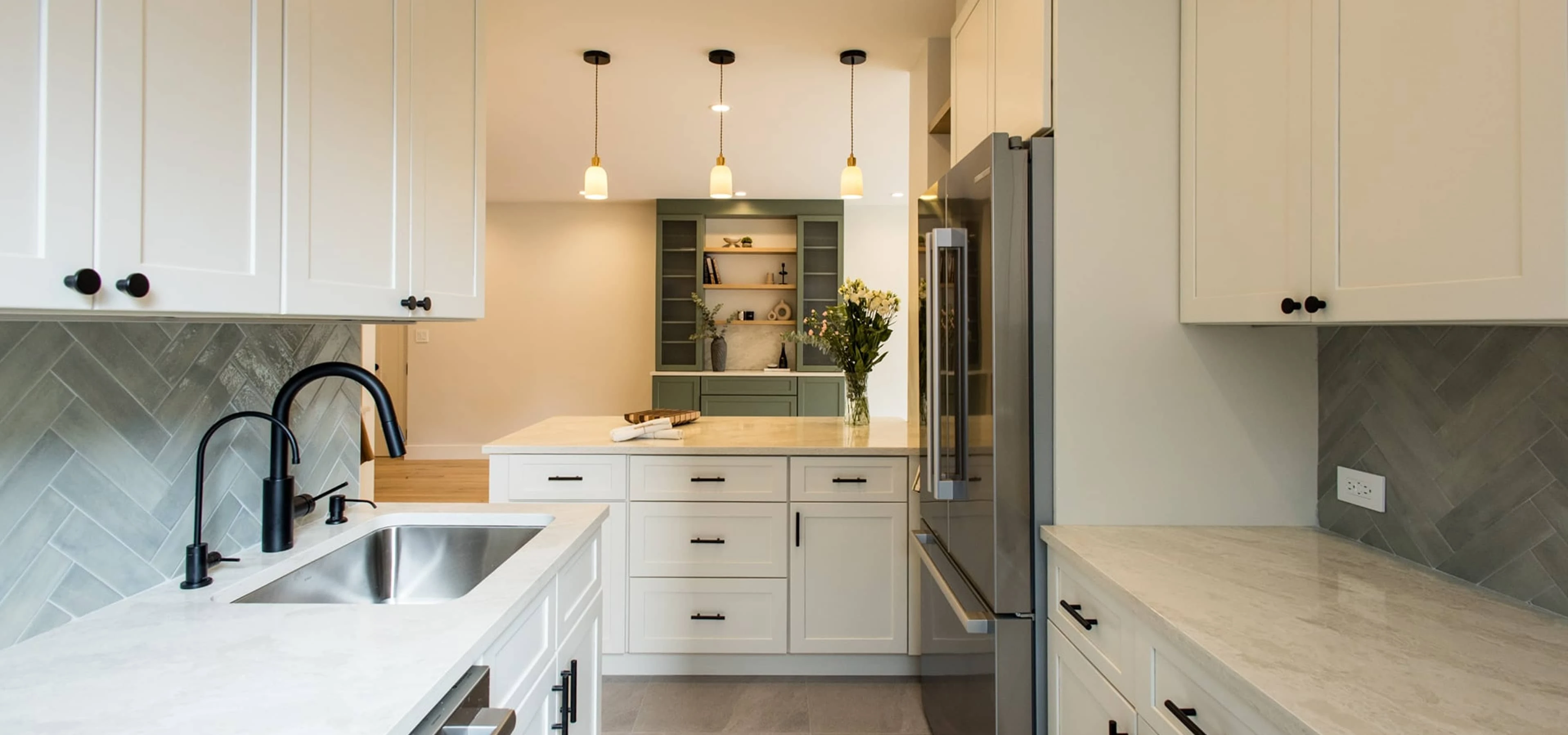 Kitchen featuring white shaker cabinets, herringbone tile backsplash, light quartz countertops, matte-black faucet, and view toward a central island with green built-in hutch and stainless-steel fridge, part of a full apartment renovation at 80 East End Avenue in Yorkville, NYC