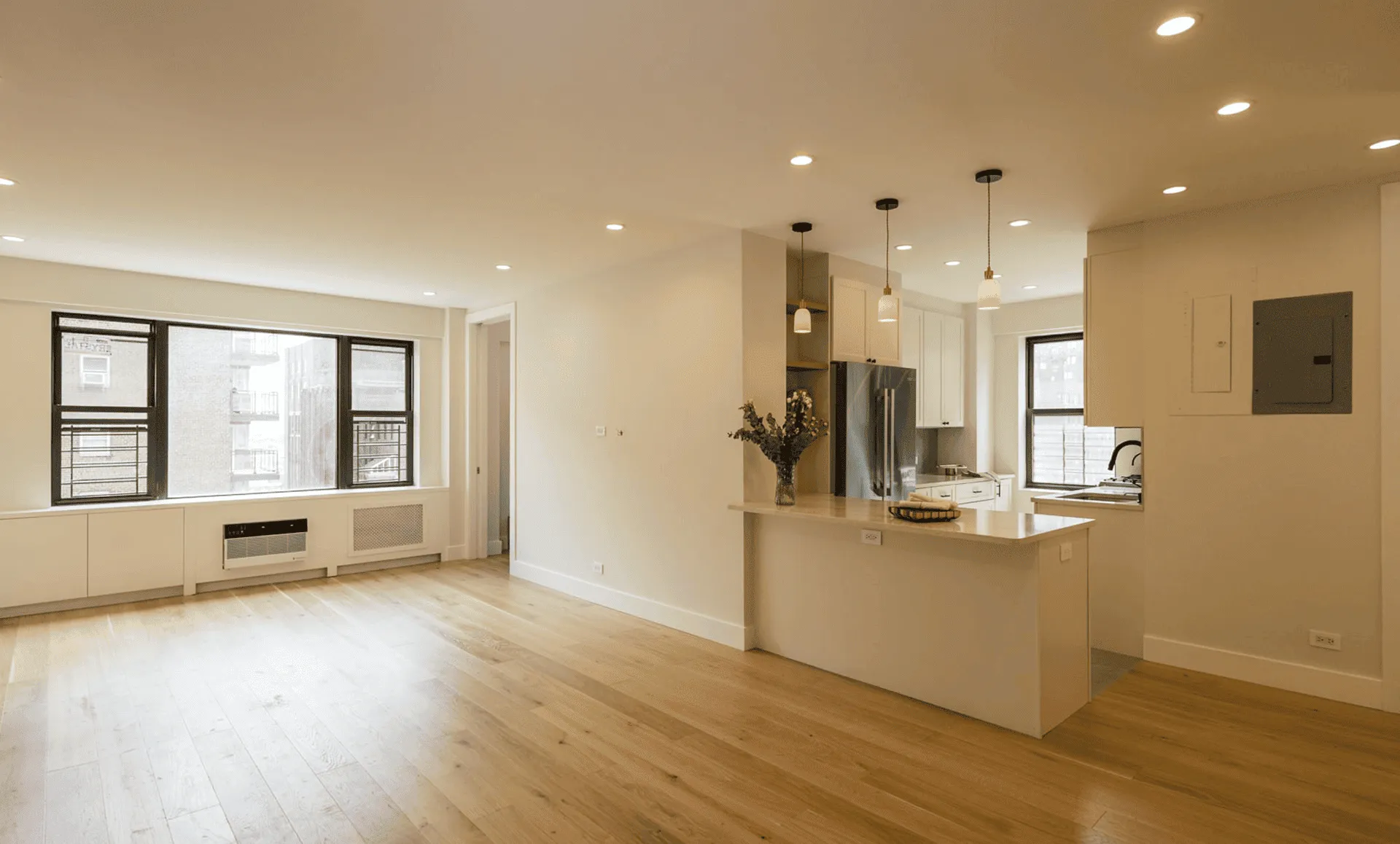 Completed living space and kitchen with light oak floor, white cabinets, island with pendant lights, and recessed ceiling lights, 80 East End Avenue Yorkville NYC