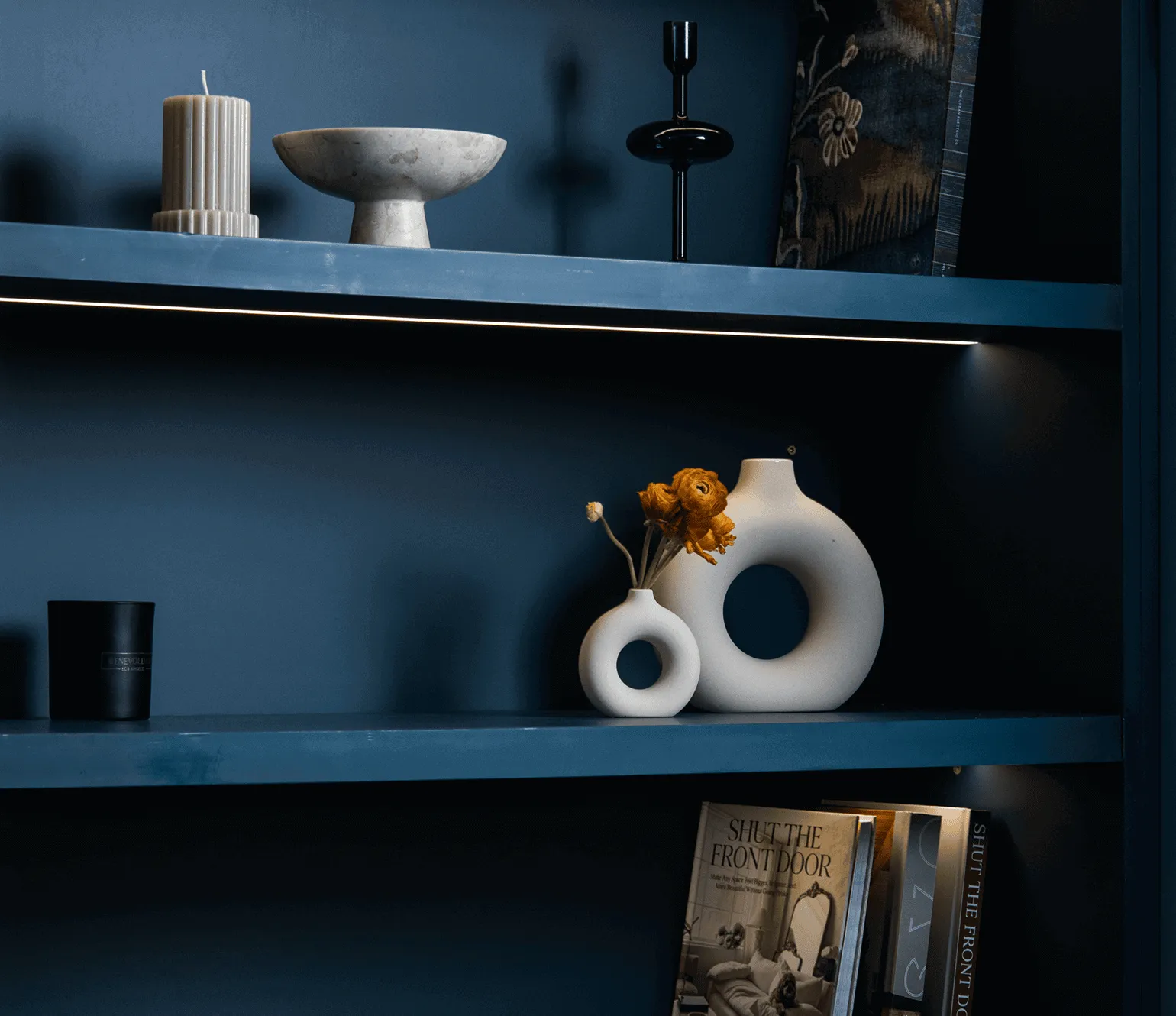 Custom open shelving with integrated lighting in renovated Jersey City apartment showing deep blue walls