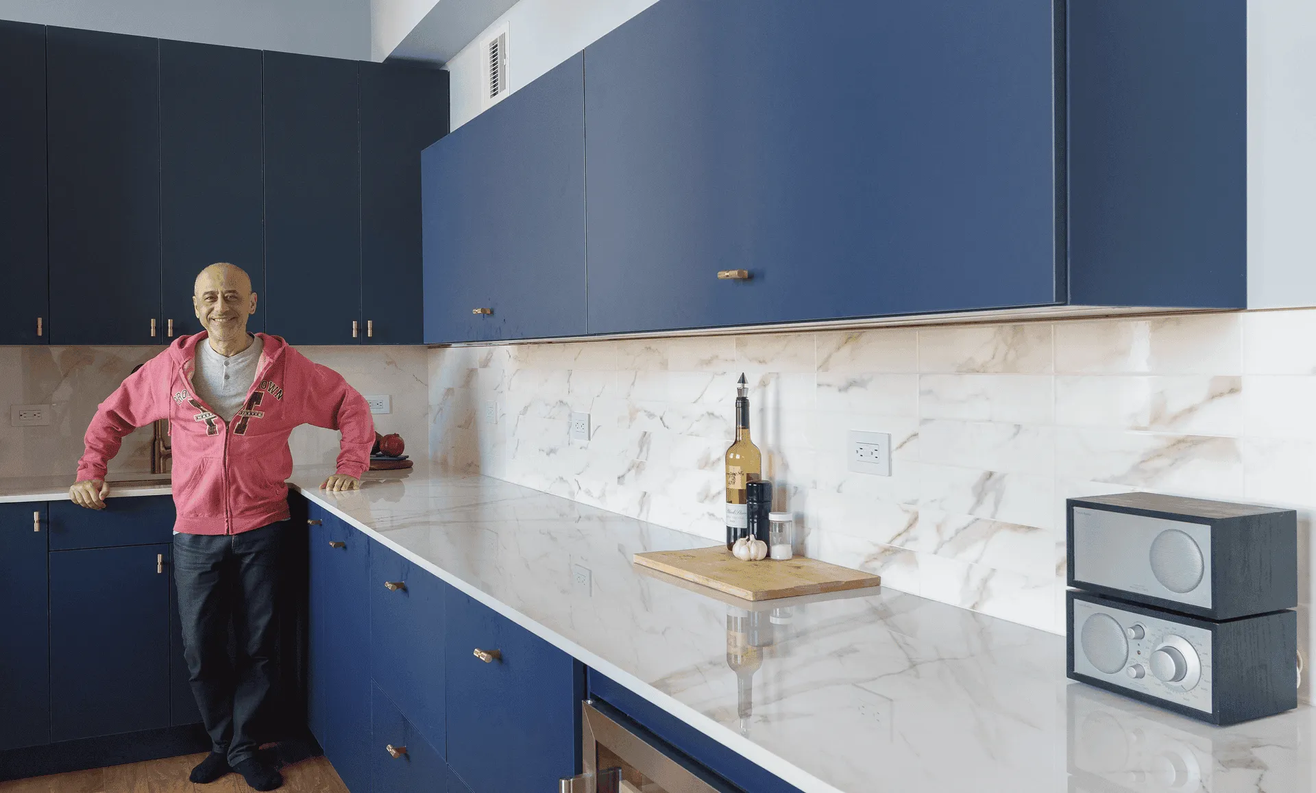 Homeowner standing in newly renovated kitchen with deep-blue flat-panel cabinets, marble-look countertop and backsplash, part of an apartment renovation at 352 W 110th St Manhattan Valley NYC