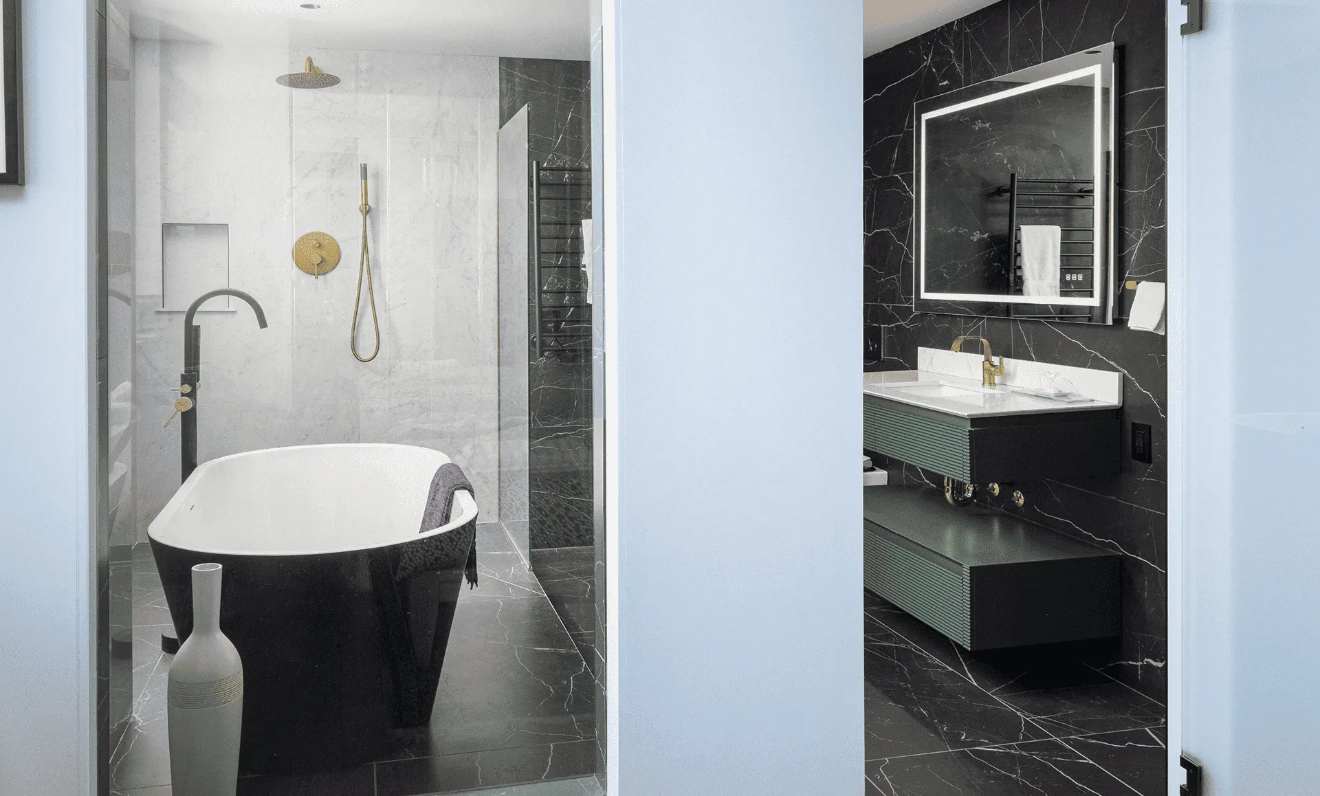 Primary bathroom view with freestanding black-rim tub, marble accent wall and brass fixtures, opening to a dark marble accent wall with illuminated mirror and green vanity, part of an apartment renovation at 352 W 110th St Manhattan Valley NYC