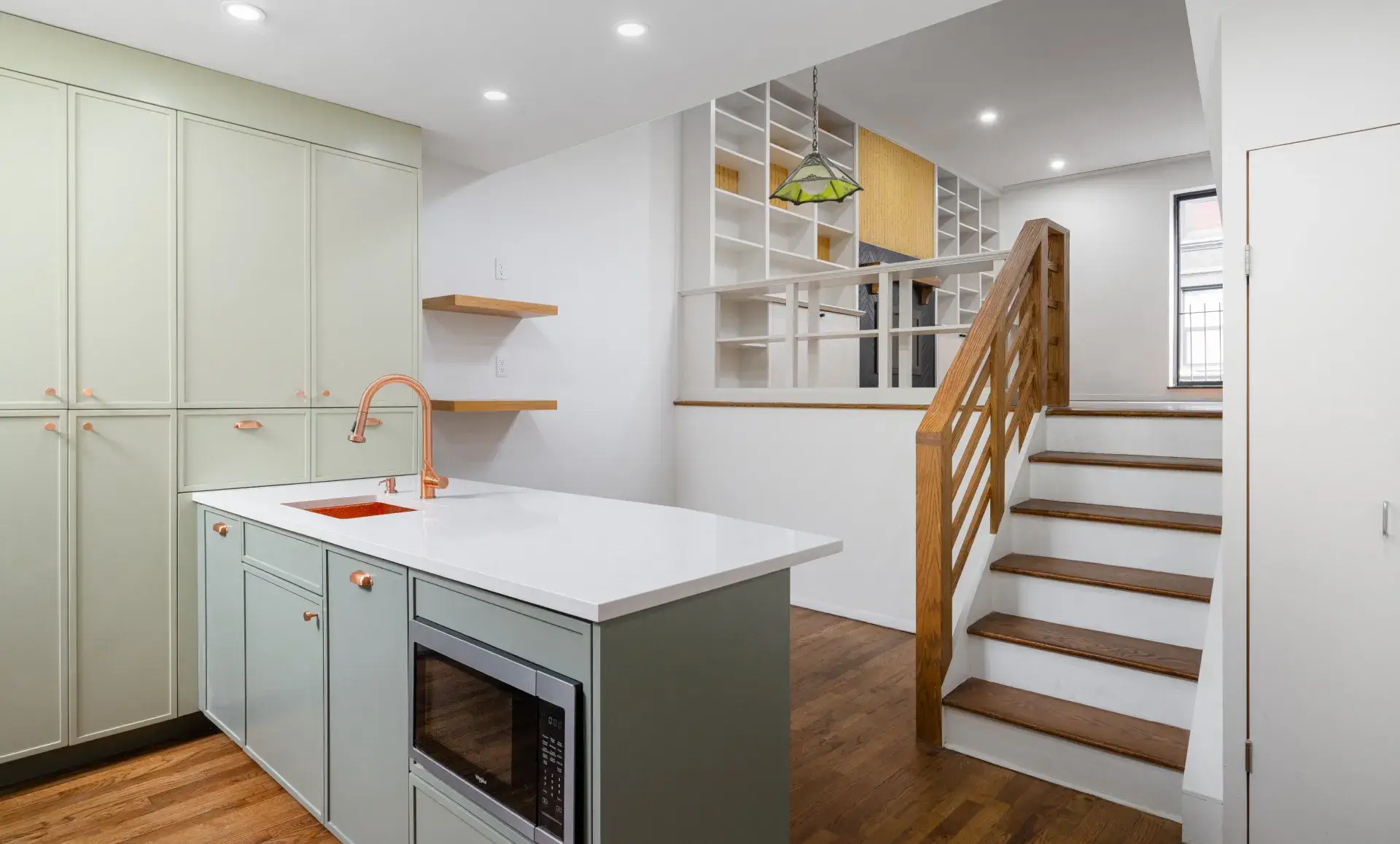 Triplex apartment renovation after photo showing custom two-tone green kitchen with copper sink